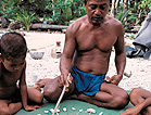 Color photograph of Mau Pialug, Micronesian wayfinder, using a star compass to teach navigation to his son who is seated to Mau's right.