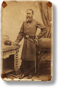 Sepia toned photograph of a bearded John Van Surly DeGrasse, circa 1863, in a military uniform standing with one hand resting on a table beside him. Courtesy Massachusetts African American Museum, Boston and Nantucket, MA and the Massachusetts Historical Society.