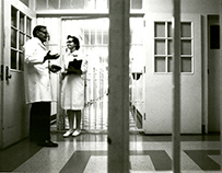 A man and woman stand speaking to one another outside a prison cell.