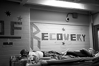 Two African American men lying in a room with the word “Recovery” on the wall.