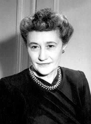 Dr. Elise Depew Strang L'Esperance, a woman in a necklace and dark blouse posing for her portrait.