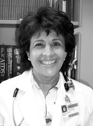 Dr. Amneris E. Luque, a woman in a lab coat and badge in front of a bookshelf.