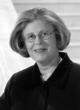 Dr. Constance Urciolo Battle, a White woman with short hair in professional attire posing on a marble staircase.