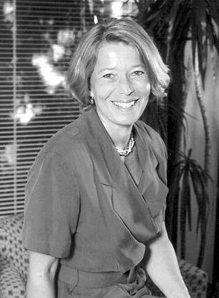 Dr. Linda Rosenstock, a White woman in a blue dress posing in an office with a table and palm tree.