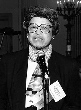 Dr. Jeanne Spurlock, an African American woman wearing a name tag and scarf speaking into a microphone.