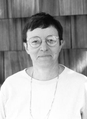 Dr. Lucy M. Candib, a White woman wearing glasses posing in front of a shingled structure.