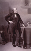 Full length, standing, of William Ferguson with his left hand resting on a table.