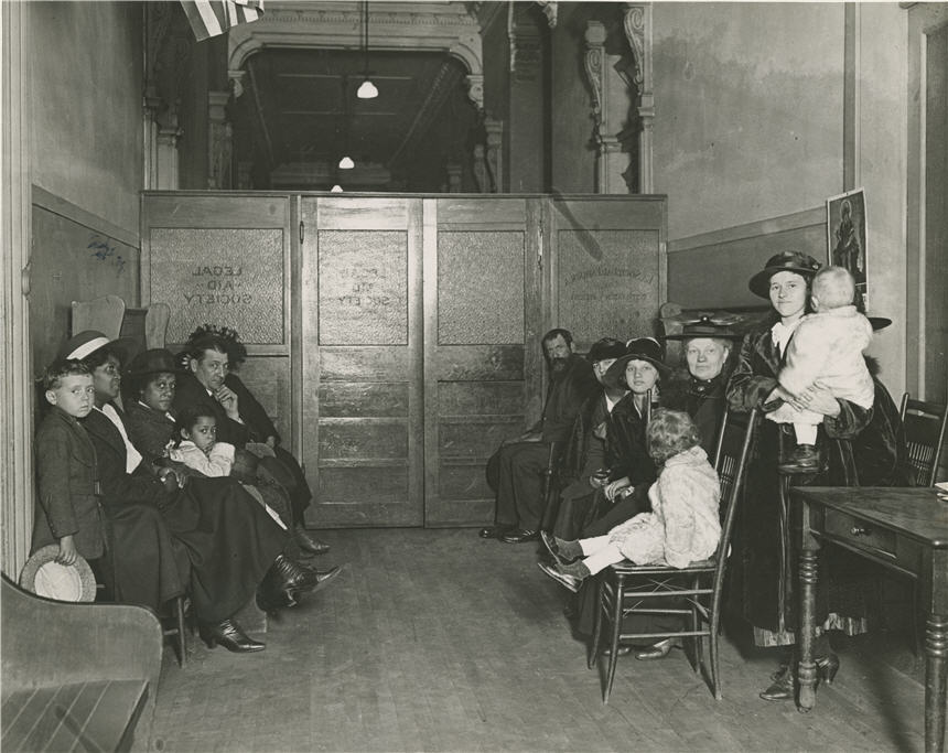 Waiting room filled with seated women and children, all looking at the viewer.
