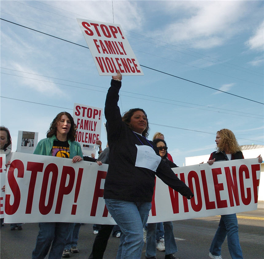 A woman holding a sign aloft leads other women holding banners and signs, marching down a street. 