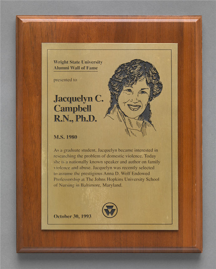 Wood and metal plaque showing bust of a White women with text underneath. 