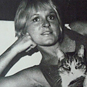 A woman lays sidewise holding cat looking at viewer. 