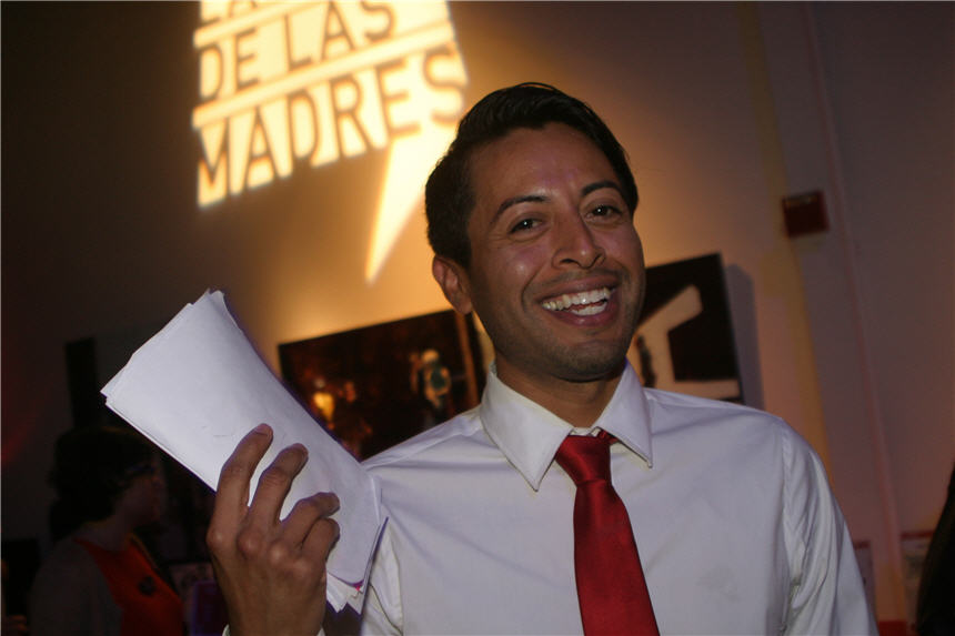 Latino man smiling holding several pieces of paper.