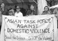 7 Asian American adults and children stand holding a banner and looking at the viewer.