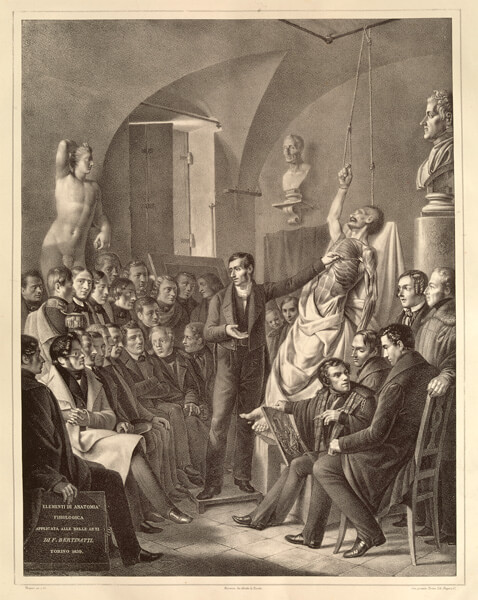 An anatomist lectures in a classroom before a partly dissected body propped up on a stand and suspended by his hand from a rope. 