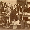Cropped photograph of the interior of an unidentified dissecting room, students pose next to three cadavers and a skeleton. United States, ca. 1910.