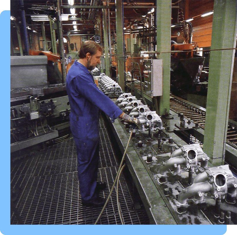 A man stands in a factory at a conveyor belt full of automobile parts