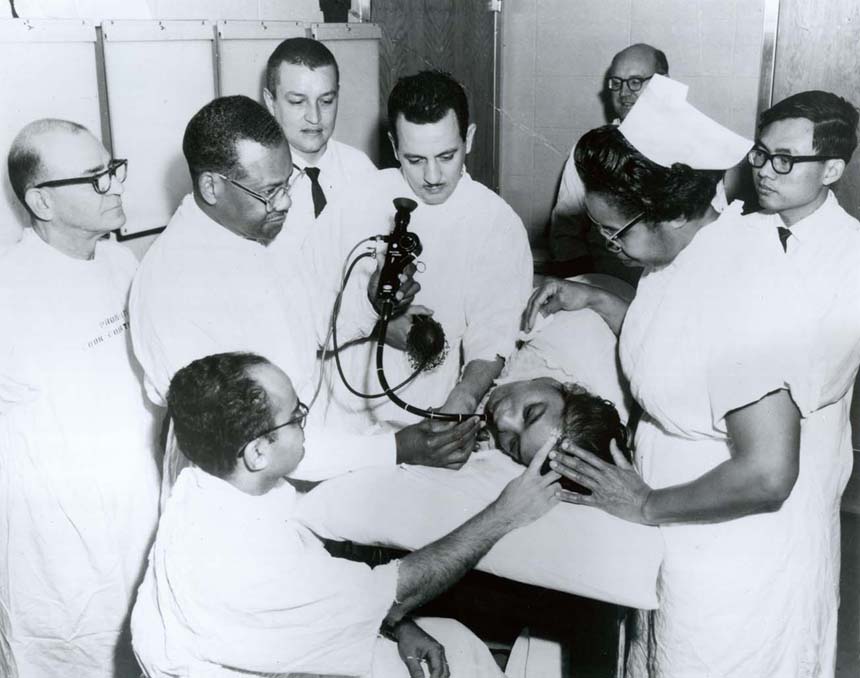Dr. Berry using a medical instrument with a group of Cook County Residents and Postgraduate students. Handwriting on back.