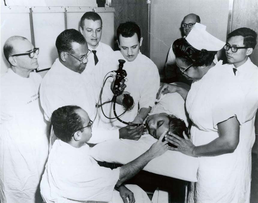 Dr. Berry using a medical instrument with a flexible tube during a teaching demonstration. Handwriting on back.