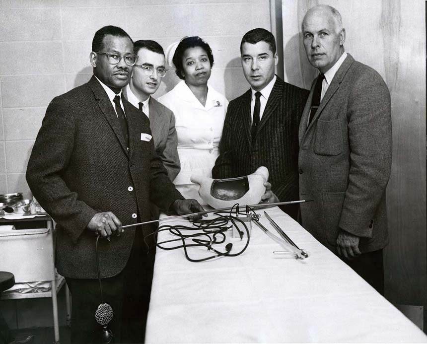 Dr. Berry holding a long rod-like tool with 3 men and a woman from the Cook County Graduate School. Handwriting on back.