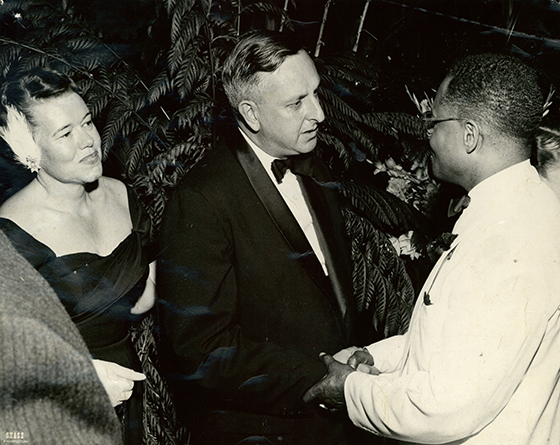 Dr. Berry in formal attire shaking hands with a white man and woman.
