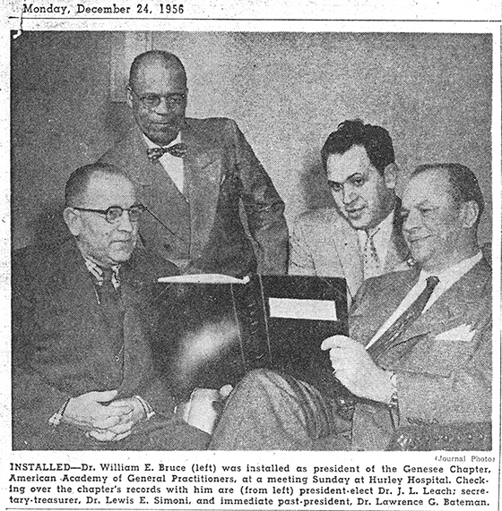 Four men sitting and looking at a book.