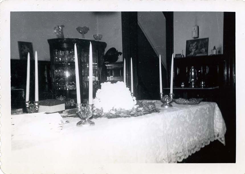 A room with a white lacy table cloth on a long table with tall candlesticks and centerpiece.