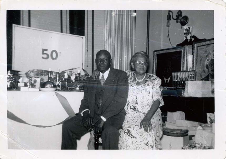 African American male and female sharing a seat in a room with presents and a long table. “50th” on the board behind the table.