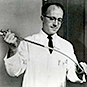 A man in a lab coat holding a long instrument with tubing in both hands.