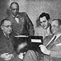 Four men sitting and looking at a book.