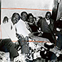Three African American males and one female, smiling, sitting on a couch with arms around each other.