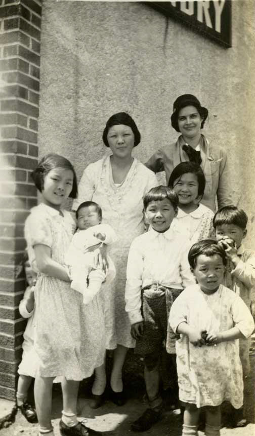 White female nurse stands with Chinese woman and seven children.