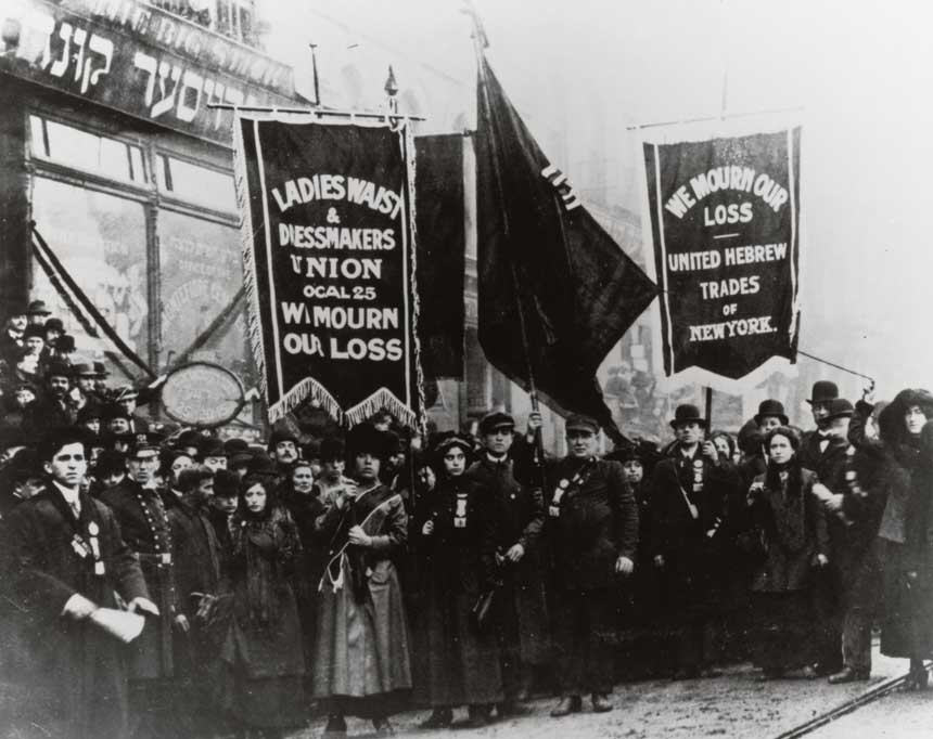 Large crowd of White men and women hold banners on a street facing the viewer.