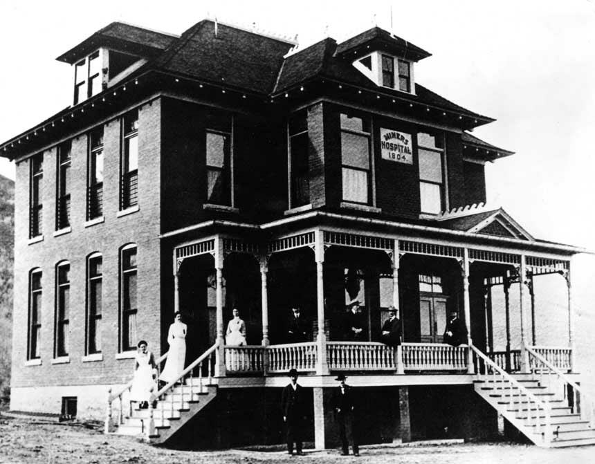 Front of a building with 9 White men and women, including nurses standing and seated on porch.