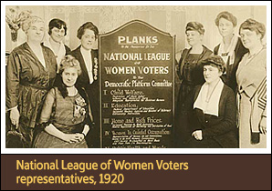 8 White women, seated and standing around a 5 foot tall board with text on it.