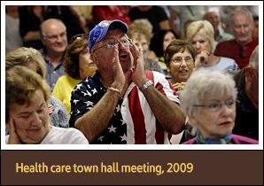 Elderly White man wearing American flag shirt cups hands to yell at speaker out of view.