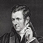 A man (Humphry Davy) seated and looking to the left resting his arm on a desk.