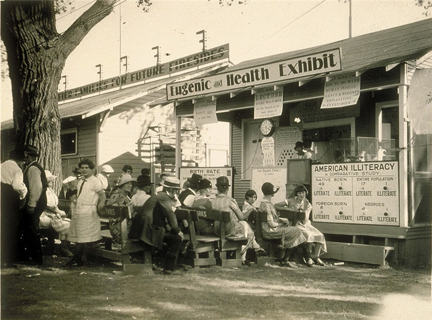 Several people sitting in chairs in front of booth titled 'Eugenic and Health Exhibit.'