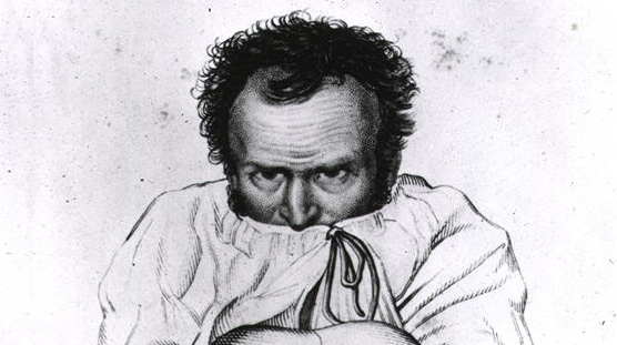 Man seated against wall with his arms wrapped around bent knees and chin buried in a straightjacket.