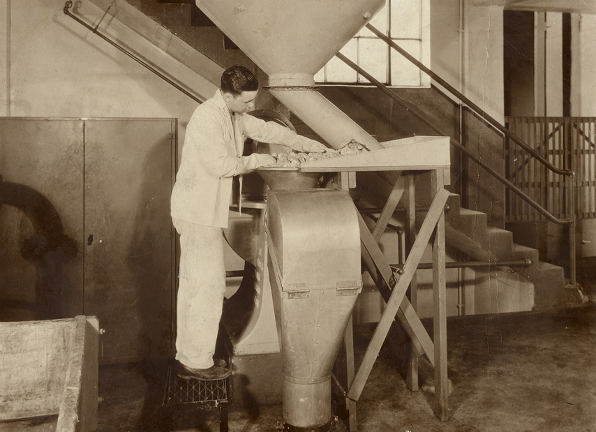A man on a stool reaching onto a platform area of a large industrial grinder.