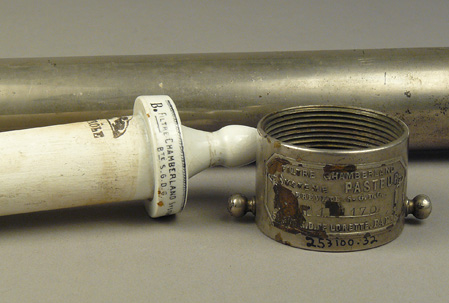 Close-up of nipple end of ceramic filter tube and cylindrical metal fitting for filter case showing manufacturer’s labels.