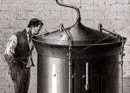 A man stands next to a large cylindrical beer vat and gazes into the vat through a small opening in the conical cover.