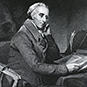 Benjamin Rush sitting at a desk turning the pages of a book and with his chin resting in his hand.
