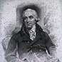 William Buchan sitting in a chair in a jacket with coiffed curly hair.