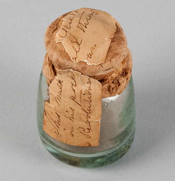 Glass bottle with browned paper label hand writing [illegible].