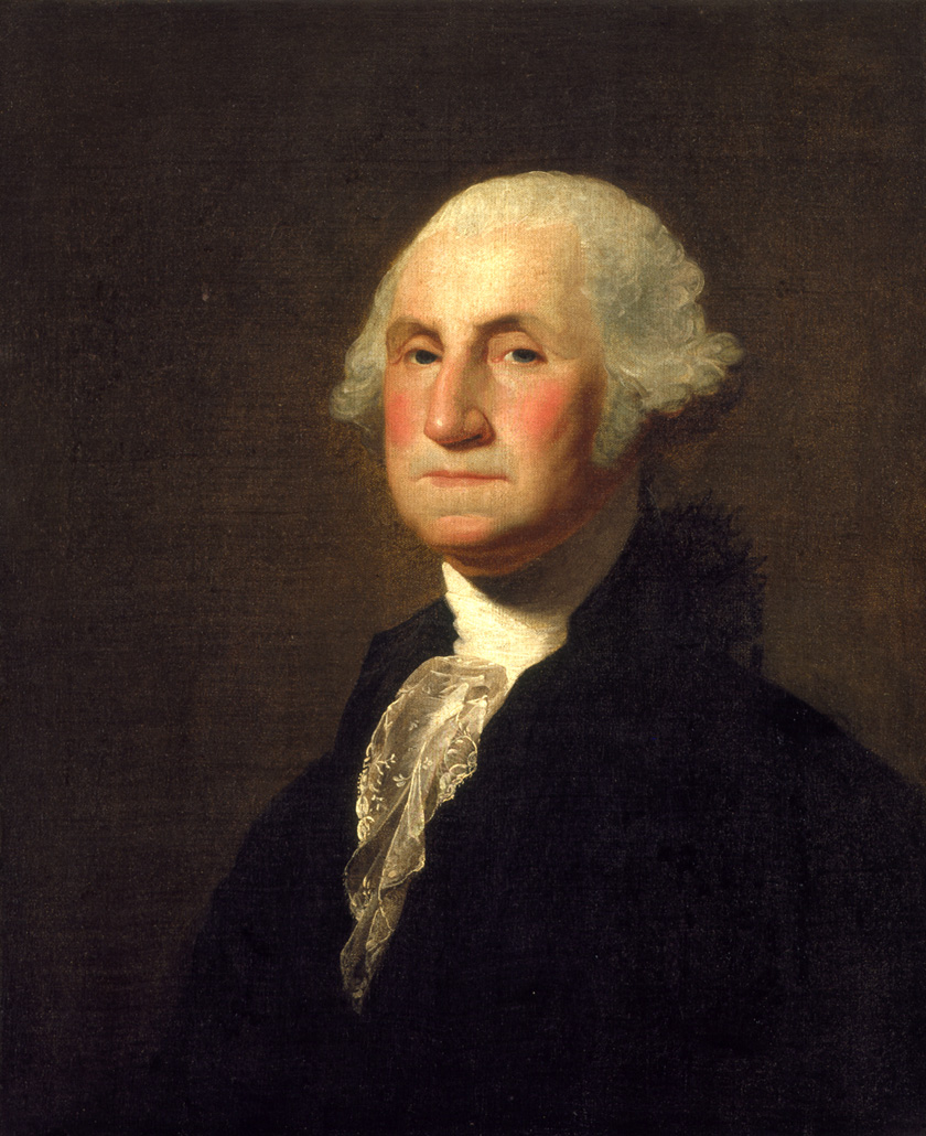 Square-jawed, white curly haired George Washington in a black jacket over a lacy white ruffle shirt.