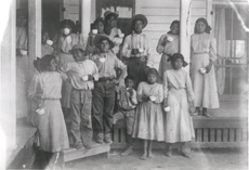 Group picture 14 Native American children standing on a porch holding cups at the Tuberculosis Sanitorium, Phoenix Indian School, Phoenix, Arizona, c. 1890-1910. Courtesy National Archives and Records Administration.