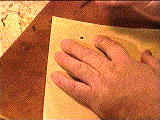 An image of Mohamed Zakariya's left hand holding down a piece of paper and holding a quill in his right hand. A black dot is in the upper right corner of the paper.