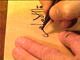 An image of Mohamed Zakariya's left hand holding down a piece of paper and holding a quill in his right hand writing on the paper.