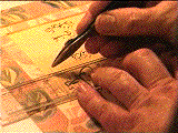 Mohamed Zakariya's left hand holding a plastic ruler down with his left hand while putting on green gold gilt on the paper with his right hand.