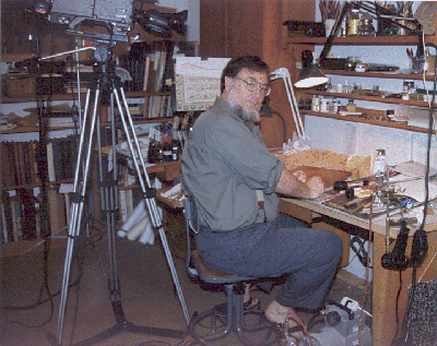 Mohamed Zakariya seated at his workbench looking over his right shoulder. A video camera is in place behind him ready for taping a session.